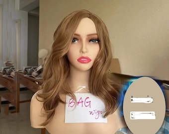 May include: A mannequin head displaying a light brown wig with long, wavy layers. The wig has a natural hairline. The mannequin has a fair complexion and is wearing makeup. A sign reading "BAG wigs" is attached to the mannequin.