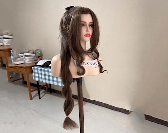 May include: A brown wig with long, wavy hair styled in a ponytail. The wig is on a mannequin head with a white face and pink lips. The mannequin head is on a wooden stand. The text "G COS" is visible on the mannequin head.