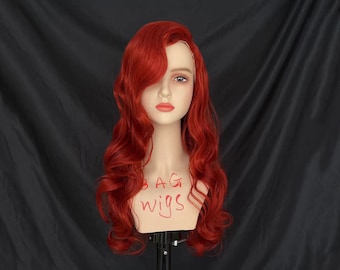 May include: A long, red, curly wig on a mannequin head. The wig is styled with a side parting and loose waves. The mannequin is wearing a black shirt.