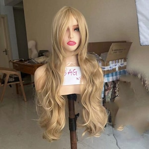 May include: A long, wavy, light blonde wig on a mannequin head. The wig is styled with loose waves and has a side parting. The wig is on a white stand with the word "BAG" written on it.