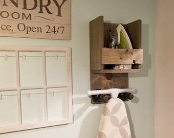 May include: A wooden wall-mounted iron holder with a white iron rest and a white ironing board hanging below. The holder has a sign that reads "Laundry Room, Service Open 24/7".
