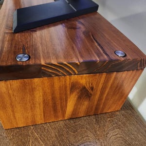 May include: A wooden box with a dark brown stain. The box has two silver screws on the top. The box is made of wood planks.