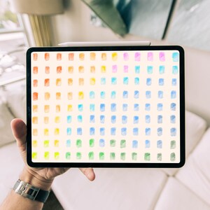 May include: A digital tablet displaying a rainbow color palette with watercolor swatches. The tablet is being held in a person's hand.