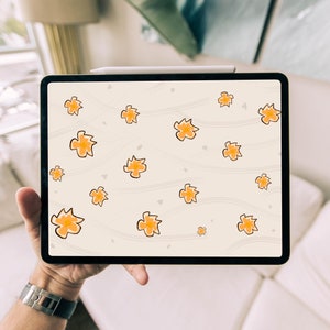Może przedstawiać: Tablet cyfrowy wyświetlający beżowe tło z wzorem pomarańczowych kwiatów. Tablet jest trzymany przez rękę.