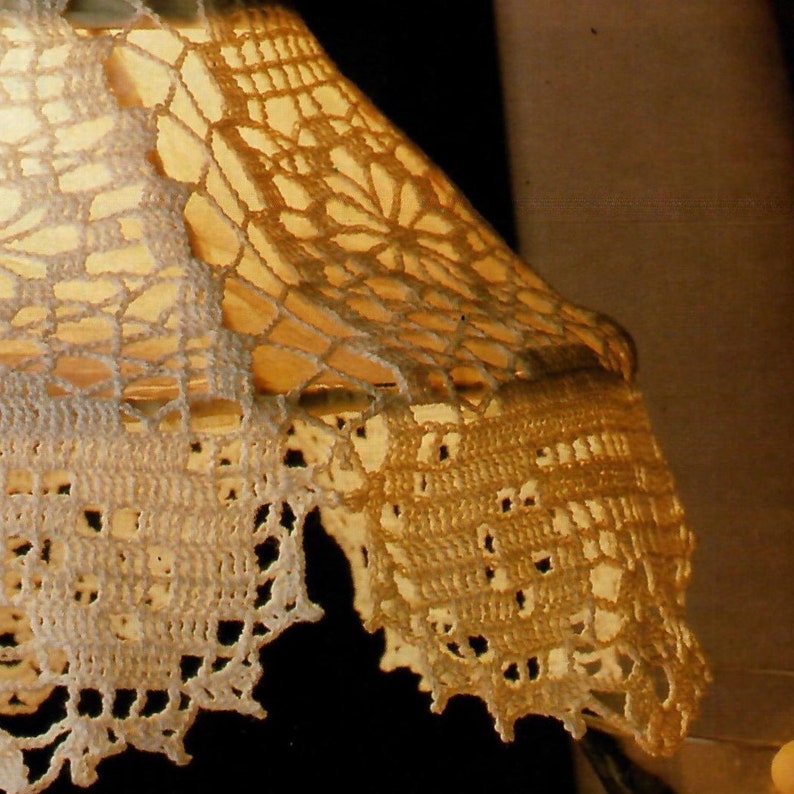 May include: A close-up of a white crocheted lampshade with a delicate floral pattern. The lampshade is lit from within, casting a warm glow.