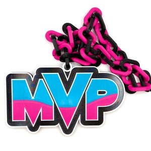 May include: A large pendant featuring the letters MVP in a bold, block font with a blue top half and a pink bottom half, outlined in black. The pendant is attached to a thick, chunky chain composed of alternating matte black and bright pink links.