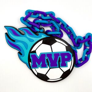 May include: A soccer-themed MVP award with a black and white soccer ball design, the letters "MVP" in purple, and a blue and purple flame design. The award is attached to a blue and purple chain.