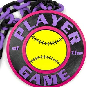 May include: A softball-themed pendant with the words "PLAYER of the GAME" in purple lettering. The pendant features a yellow softball design with black stitching, set against a black background with a pink border. A purple and black chain is attached.