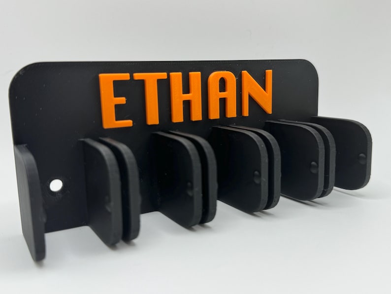 May include: Black wall mounted organizer with the name 'custom' in orange letters. The organizer has six slots for storing items.