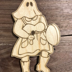 May include: A wooden cutout of a ghost wearing a dress and boots, holding a microphone and a round object.