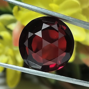 May include: A deep red gemstone with a faceted cut. The gemstone is round and has a high polish.