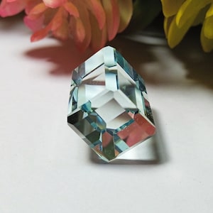 Puede incluir: Una piedra preciosa azul claro con forma cuadrada facetada. La piedra preciosa está tallada en un estilo geométrico único.