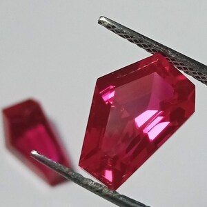 May include: Two red gemstone pendants with a faceted, coffin-shaped cut. The pendants are held by a pair of tweezers.