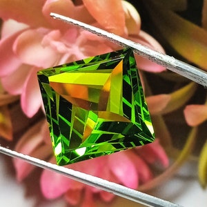 Peut inclure: Une pierre précieuse verte et jaune de forme carrée et taillée à facettes. La pierre précieuse est tenue dans une pince.