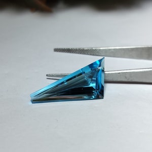 Op de afbeelding: Een driehoekige, gefacetteerde edelsteen met een blauwe tot turquoise kleur.