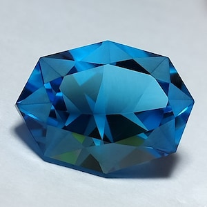 May include: A large, faceted, blue gemstone with an octagonal shape. The gemstone is cut to create a brilliant, sparkling effect.