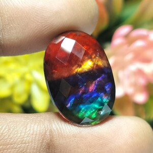 May include: An oval gemstone with a faceted cut, displaying a multi-coloured pattern of red, orange, yellow, blue, green and purple.