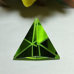 Peut inclure: Une pyramide en verre vert avec un design facetté. La pyramide a une pointe acérée et une base triangulaire.