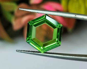 以下が含まれることがあります： ピンセットで保持された六角形の明るい緑色の宝石。宝石はファセットデザインでカットされています。