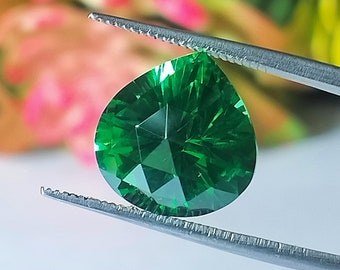 Op de afbeelding: Een peervormige groene edelsteen met een facetgeslepen vorm, vastgehouden door een pincet tegen een wazige achtergrond.