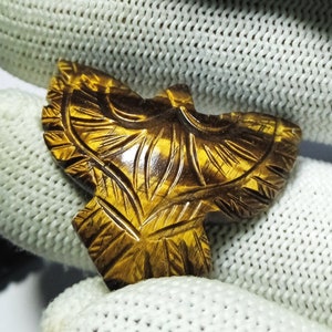May include: A carved tiger's eye gemstone pendant in the shape of a bird with intricate details. The pendant is a rich golden brown color with a glossy finish.