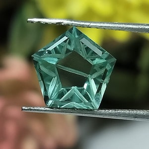 Può includere: Una pietra preziosa verde a forma di stella con taglio sfaccettato. La pietra preziosa è tenuta da una pinzetta.