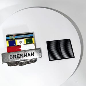May include: A silver and black enamel military pin with a red, white, and blue ribbon and the text "DRENNAN" and "SERVICE 2016 SINCE".