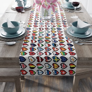 May include: White table runner with a pattern of colorful hearts featuring flags from different countries. The runner is on a wooden table with two place settings on each side.