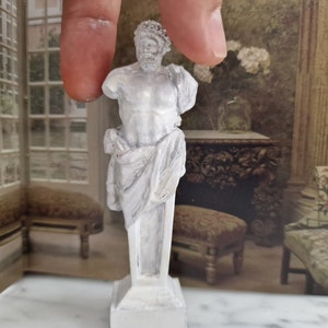 Puede incluir: Estatua de yeso blanco de un torso masculino con una tela drapeada, de pie sobre un pedestal blanco. La estatua es una reproducción de una escultura griega clásica.