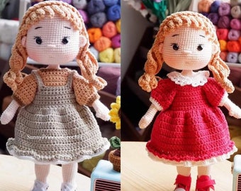 May include: Two crocheted dolls with long blonde hair wearing dresses. One doll is wearing a brown dress with a white lace trim and the other doll is wearing a red dress with a white lace trim.