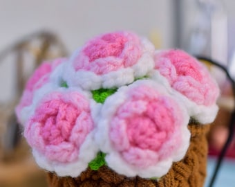 May include: A crocheted flower arrangement in a brown pot. The flowers are pink and white with green leaves. The pot has a woven texture. The text "Sunny Princess Crochet" is visible on the pot.