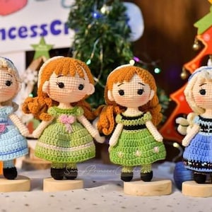 Puede incluir: Cuatro muñecas de crochet vestidas con vestidos azules y verdes con cabello rubio y castaño. Las muñecas están de pie sobre bases de madera. Las muñecas están hechas a mano y son una gran adición a cualquier decoración del hogar.