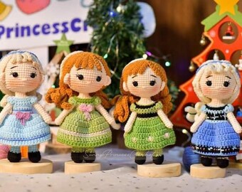 May include: Four crocheted dolls dressed in blue and green dresses with blonde and brown hair. The dolls are standing on wooden bases. The dolls are handmade and are a great addition to any home decor.
