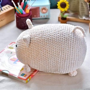 May include: White crocheted stuffed animal shaped like a pig. The pig has a small tail and two small ears.
