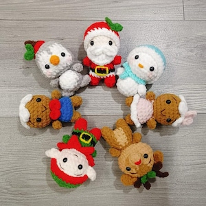May include: A collection of handmade crochet Christmas ornaments. The ornaments include a snowman, Santa Claus, a gingerbread person, an elf, a reindeer, and a second snowman. Each ornament is made with colorful yarn and has a unique design.