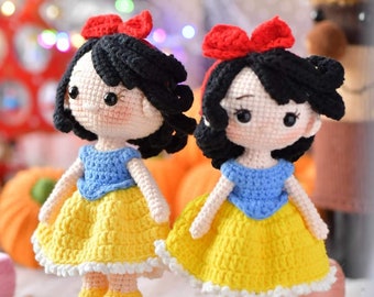 May include: Two crocheted Snow White dolls with black hair, red bows, yellow dresses, and blue tops. The dolls are standing on wooden bases.