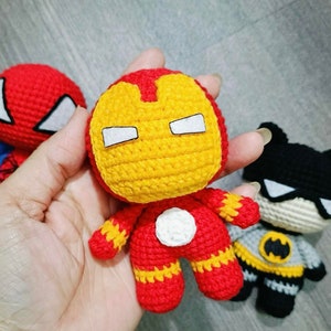 Op de afbeelding: Drie gehaakte superhelden speelgoedjes: een rode en blauwe Spiderman, een gele en rode Iron Man en een zwarte en grijze Batman.
