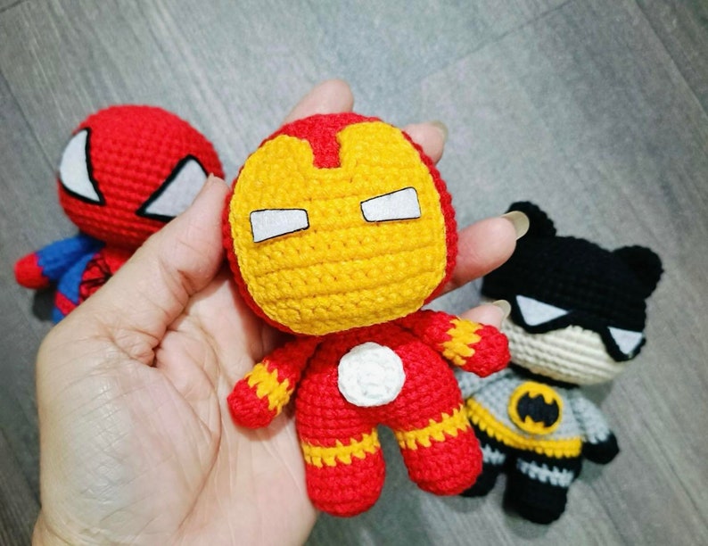 Puede incluir: Tres juguetes de superh&eacute;roes de crochet: un Spiderman rojo y azul, un Iron Man amarillo y rojo y un Batman negro y gris.