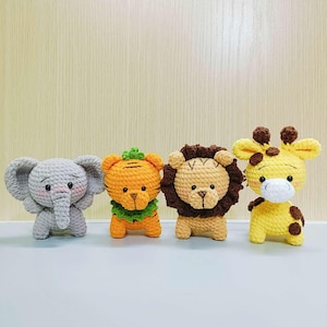 May include: Four crocheted stuffed animals: a gray elephant, an orange tiger, a brown lion, and a yellow giraffe. The animals are all standing on a light gray surface.