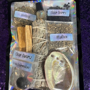Może przedstawiać: Przezroczysta plastikowa torba zawierająca różne przedmioty duchowe. Zawiera wiązki szałwii, patyczki palo santo, małą butelkę olejku eterycznego, wypolerowaną muszlę ucha morskiego oraz paczki z etykietami "Hyssop", "Elder Berry", "Mullien", "Clear Quartz" i "Black Tourmaline".