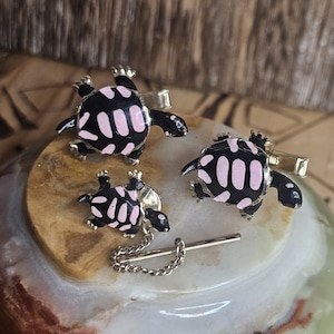 May include: A set of three turtle cufflinks and a tie tack. The turtles are black with pink accents and have a gold finish.