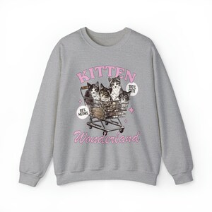 Puede incluir: Sudadera gris con un gr&aacute;fico rosa de cuatro gatitos en un carrito de compras. El gr&aacute;fico dice "Kitten Wonderland" e incluye el texto "99% Meows" y "100% Cute".
