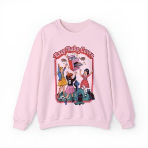 May include: Pink sweatshirt with a graphic print of three girls in front of an Easy-Bake Oven. The text "Easy-Bake Coven" is above the oven.