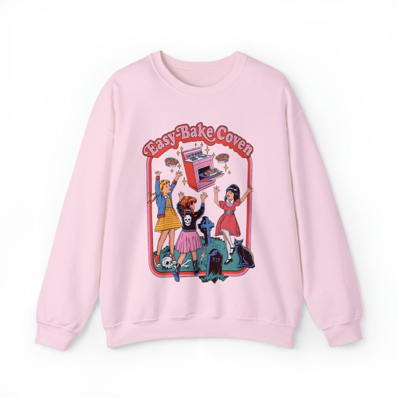 May include: Pink sweatshirt with a graphic print of three girls in front of an Easy-Bake Oven. The text "Easy-Bake Coven" is above the oven.