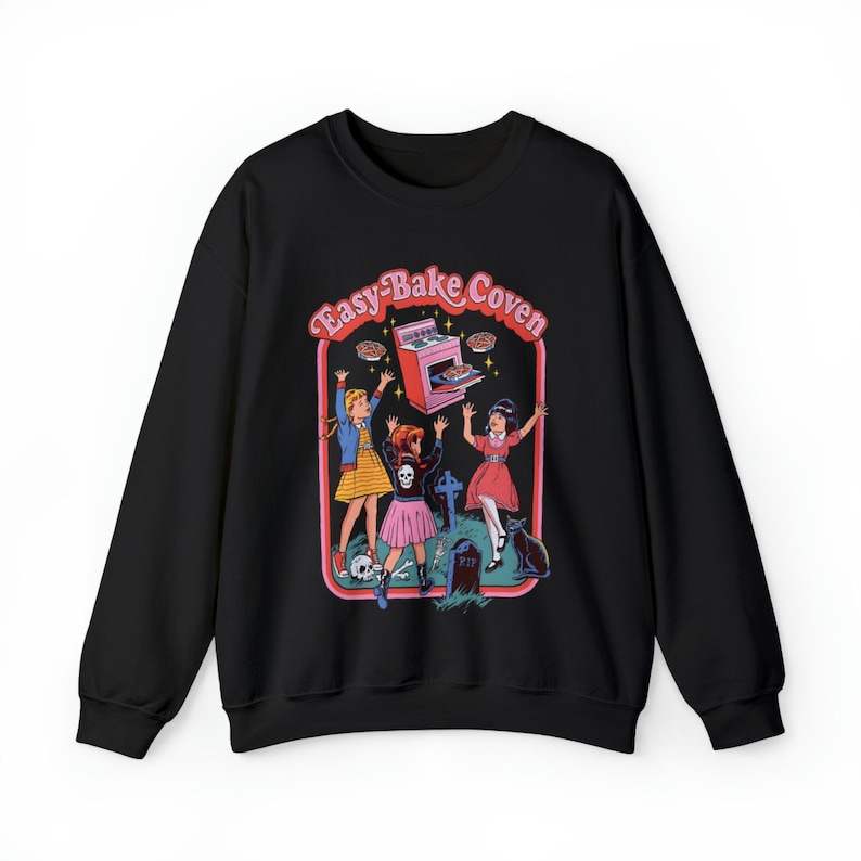 May include: Black sweatshirt with a graphic print of three girls in front of an Easy-Bake Oven. The text "Easy-Bake Coven" is above the oven. The girls are wearing pink and blue dresses and holding pies. A black cat is in the background.
