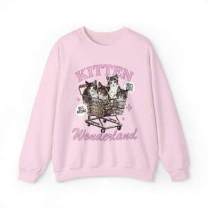 Puede incluir: Sudadera rosa con un gr&aacute;fico de cuatro gatitos en un carro de la compra. El texto "Kitten Wonderland" est&aacute; impreso debajo de la imagen. El texto "99% Meows" est&aacute; impreso en el lado izquierdo de la imagen y "100% Cute" est&aacute; impreso en el lado derecho de la imagen.