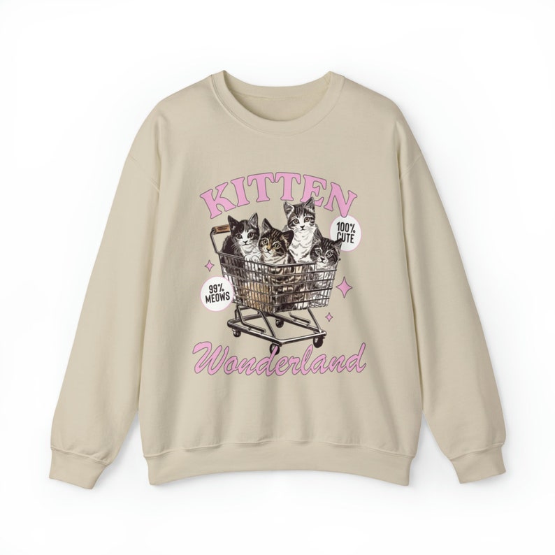 Puede incluir: Sudadera beige con un estampado gr&aacute;fico de cuatro gatitos en un carro de la compra. El texto "Kitten Wonderland" est&aacute; impreso debajo de la imagen. Los textos "99% Meows" y "100% Cute" est&aacute;n impresos en el gr&aacute;fico.