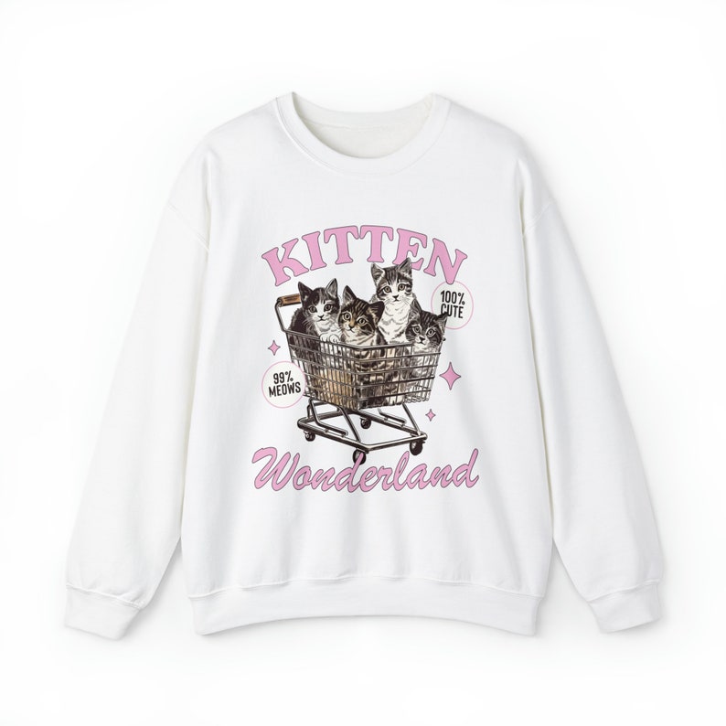 Puede incluir: Sudadera blanca con un estampado gr&aacute;fico rosa de cuatro gatitos en un carrito de la compra. El texto del gr&aacute;fico dice "Kitten Wonderland" y "99% Meows" y "100% Cute".
