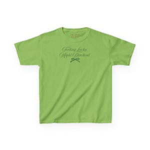 May include: A lime green t-shirt with the text "Feeling Lucky, Might Blackout" in a script font. The shirt has a crew neck and short sleeves. The text is in a dark green color. The brand name "The Luxe Designs" is at the top.