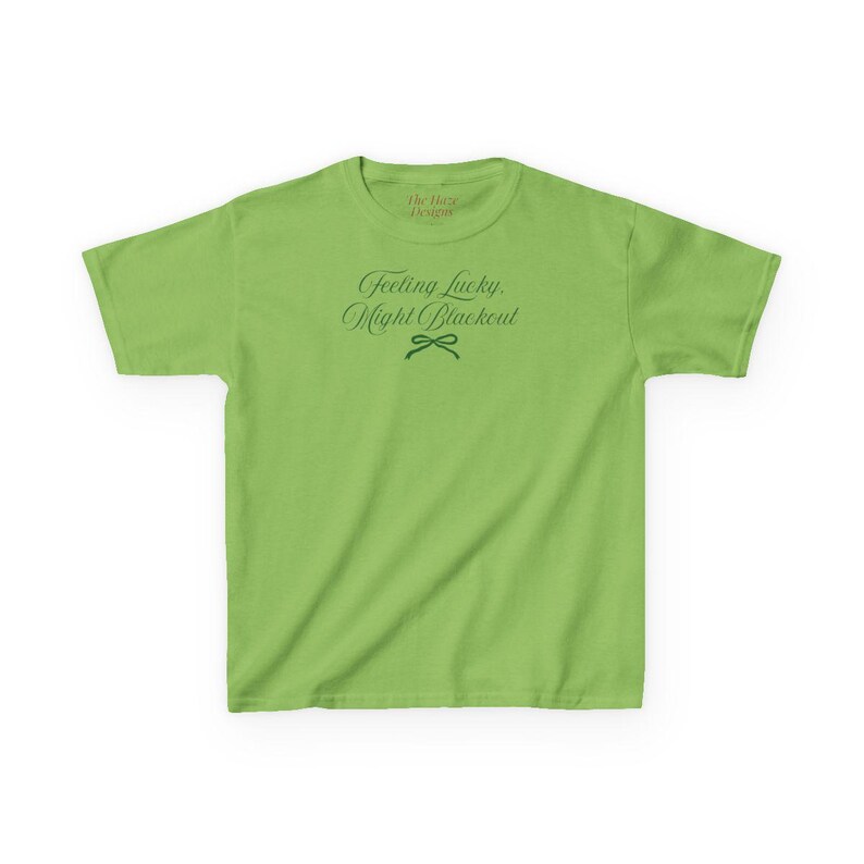 May include: A lime green t-shirt with the text "Feeling Lucky, Might Blackout" in a script font. The shirt has a crew neck and short sleeves. The text is in a dark green color. The brand name "The Luxe Designs" is at the top.